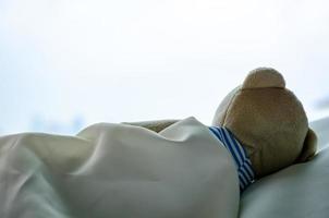 Teddy bear sleeping alone on bed facing to window in the lonely day. photo