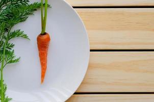 Fresh organic baby carrot with its tree on white plate with wooden background. photo