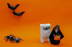 The origami Halloween background of the nun holding pumpkin head jack o lantern and mummy run away from bats and spiders isolated on orange background. photo