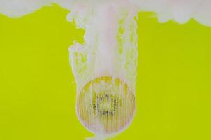 Blurred focus of dissolving pink poster color in water with slice kiwi fruit on yellow background photo