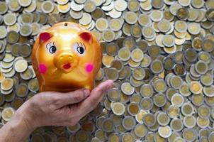 Hand holding piggy bank on blurred background of Thai baht coins. Money saving concept. photo