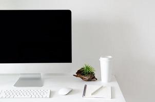 pantalla de computadora personal moderna en mesa blanca con una taza de café y planta de aire tillandsia con espacio para texto en pared blanca para trabajo y concepto de oficina.