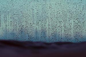 Rain drop on glass window in monsoon season with blurred blanket on bed and city background. photo