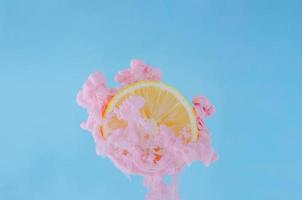 Slice lemon with partial focus of dissolving pink poster color in water on blue background for summer, abstract and background concept. photo