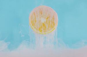 Blurred focus of dissolving pink poster color in water with slice lemon on blue background for summer, abstract and background concept. photo