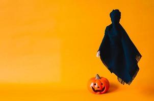 Black ghost sheet flying on orange background with blurred pumpkin on the floor. Halloween minimal concept. photo