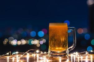 A glass of beer on wooden table with colorful city bokeh light background. photo