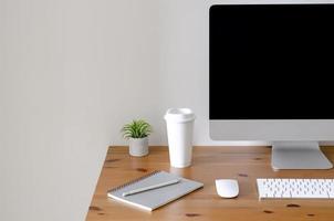 pantalla de computadora personal moderna en una mesa de madera con una taza de café y planta de aire tillandsia con espacio para texto en una pared blanca para el concepto de trabajo y oficina. foto