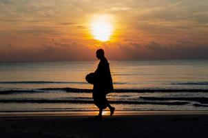 Sunrise with reflection on the sea and beach that have blurred silhouette photo of buddhist monk.