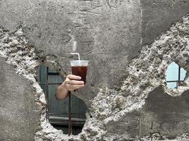 mano sujetando café helado del hueco de rotura de la antigua muralla. concepto de bebida de verano. foto