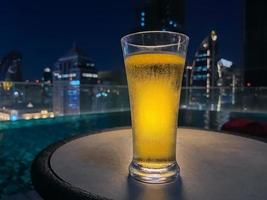 A glass of beer puts on table at rooftop bar with colorful city background. photo