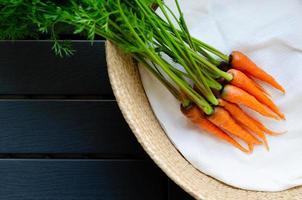 un montón de zanahorias orgánicas frescas con sus árboles puestos en una cesta con tela blanca y un fondo oscuro. foto