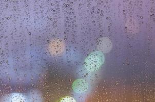 Rain drop on glass window in monsoon season with colorful bokeh light photo