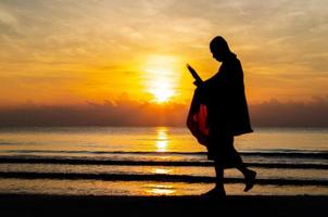 Sunrise with reflection on the sea and beach that have blurred silhouette photo of buddhist monk.