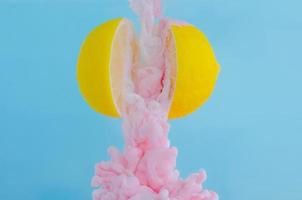 Partial focus of dissolving pink poster color in water drop between two slice lemons on blue background photo