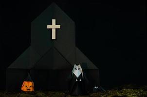The Halloween background of origami or Paper folding that the nun standing in front of black church with jack o lantern and spider with messy lawn on black background. photo