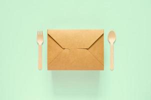caja de comida de papel desechable y compostable, tenedor y cuchara sobre fondo verde para el concepto del día mundial del medio ambiente. foto