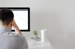 A person working with serious expression at office with personal computer screen that have a coffee and tillandsia air plant with space for text on white wall for working and office concept. photo