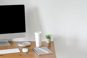 Modern personal computer screen on wooden table with a cup of coffee and Tillandsia air plant with space for text on white wall for working and office concept. photo