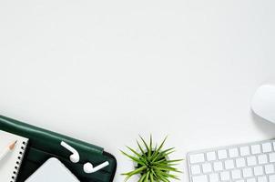 Modern workplace with wireless keyboard and mouse, smartphone with wireless earphones, pencil, notebook, green document bag and Tillandsia air plant on white background. Top view, flat lay concept. photo