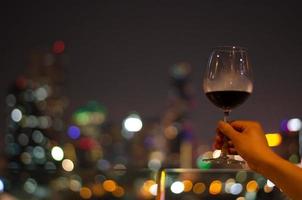 Hand holding and toasting a glass of red wine at the rooftop bar. photo