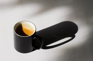 A black cup of hot coffee put on white table with shadow photo