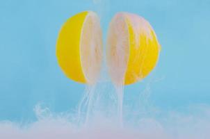 Blurred focus of dissolving pink poster color in water drop between two slice lemons on blue background photo
