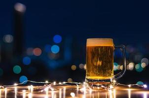 A glass of beer on wooden table with colorful city bokeh light background. photo