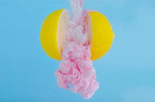 Partial focus of dissolving pink poster color in water drop between two slice lemons on blue background for summer, abstract and background concept. photo