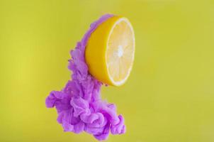 Slice lemon with partial focus of dissolving violet poster color in water on yellow background for summer, abstract and background concept. photo
