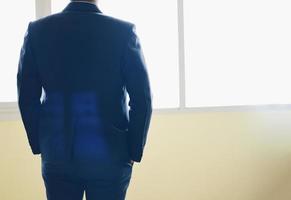 Business man standing and looking at window - Back view of successful manager looking the city from his office photo