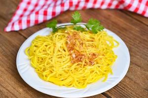 yellow noodles on white plate and wooden background , instant noodles yellow noodles rice vermicelli food with fried garlic and coriander photo