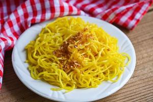 yellow noodles on white plate and wooden background , instant noodles yellow noodles rice vermicelli food with fried garlic photo