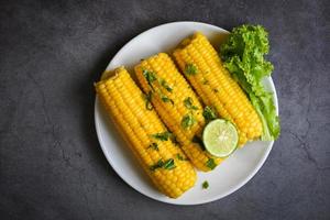 comida de maíz dulce con ensalada de verduras, lima, cilantro y lechuga, maíz dulce cocido en un plato blanco, mazorcas de maíz maduras al vapor o hervidas para la cena o merienda vegana foto