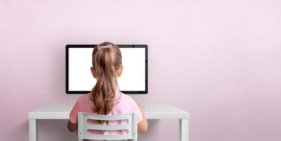 Girl sitting on a chair and working on the computer. Isolated computer display for design promotion. Pink wall with copy space photo