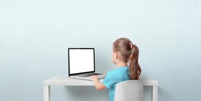 Young girl using laptop computer in living room. Isolated laptop display for web page promotion. Back view. Copy space on wall photo