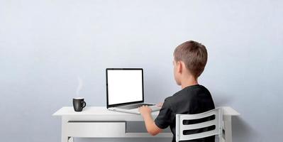 Young boy working on the laptop computer. Notebook with isolated display for web page promotion. Back view with copy space on wall photo