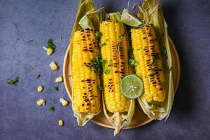 sweet corn food with lime and coriander , sweet corn cooked on plate background, ripe corn cobs grilled sweetcorn for food vegan dinner or snack - top view photo