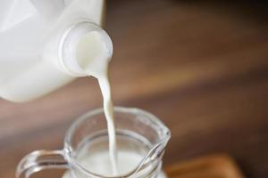 Fresh milk natural in bottle and  Pouring milk into glass jug on wooden background - photo