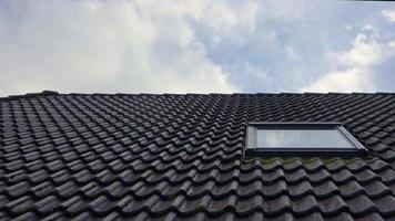 Zeitrafferaufnahme von Wolken, die sich im Fenster eines Wohnhausdachs mit schwarzen Ziegeln spiegeln. video