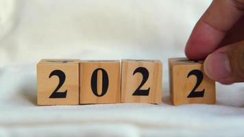 The wooden cubes in a row are numbered 2022. Male hand transforms 2022 into 2023 video