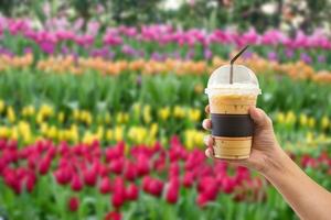 women hand holding the iced coffee with blur flower garden background photo