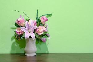 lirio rosa y rosa en jarrón sobre mesa de madera con fondo de pared verde foto