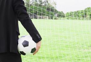 Soccer team manager is holding ball with goal net and green grass field background photo