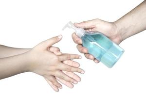 Closeup of father hand pushing alcohol sanitizer gel pump dispenser to son hand isolated over white background - people with alcohol sanitizer prevent bacteria and COVID-19 virus protection concept. photo