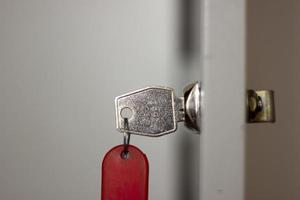 Metal office key with red fob in lock closeup, horizontal photo on blurred background. Open door with key, safety system for document files and information