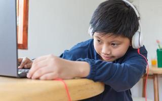 Asian cute boy reaches out to plug his headphones into his laptop by himself with a face that intends to use the computer to study online at home. link and connect photo