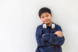 lindo chico asiático en una sudadera con capucha posando de pie sonriendo con los brazos cruzados en un gesto feliz y seguro usando auriculares aislados sobre fondo blanco.retrato infantil y estilo de vida foto