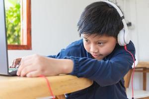 Asian cute boy reaches out to plug his headphones into his laptop by himself with a face that intends to use the computer to study online at home. link and connect photo