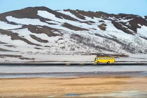 A yellow local bus driving on the road with the beautiful landscape in Myvatn region of Northern Iceland. photo